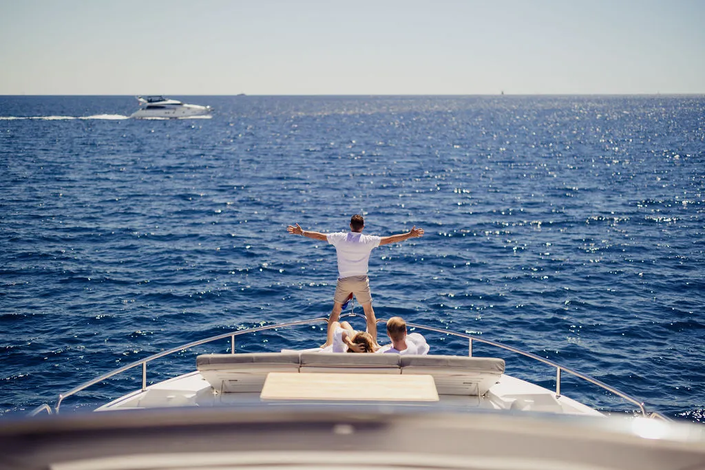 Charter-Gast streckt die Arme zum Himmel auf dem Bug einer Yacht vor Mallorca — das Lebensgefühl, das JH Lifestyle einfängt
