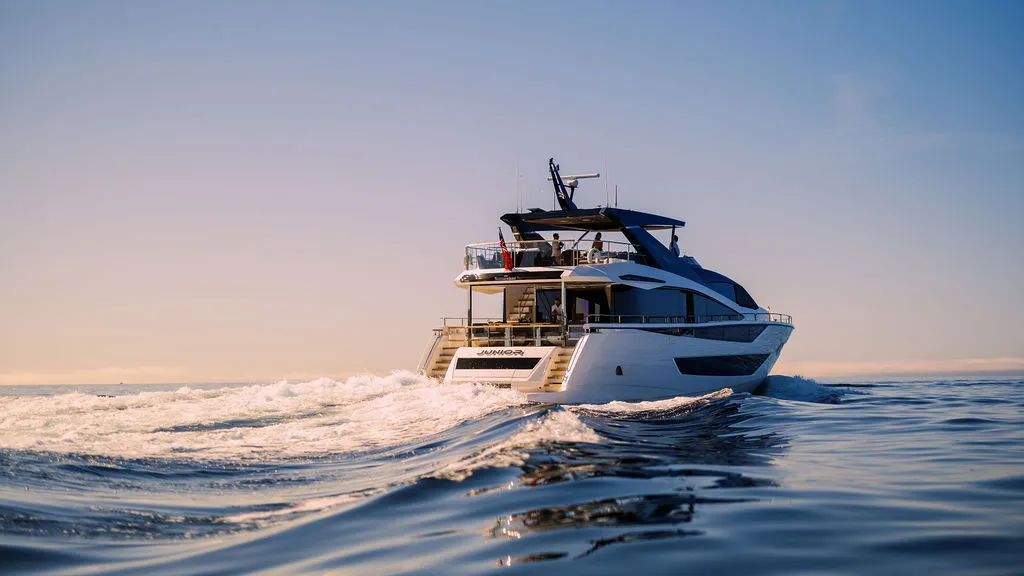 Superyacht JUNIOR vor Mallorca in der goldenen Stunde — Heckansicht mit beleuchteter Badeplattform vor der Küste der Tramuntana, vermittelt durch Yachtmakler Julian Hoeke